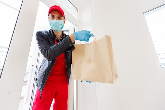 delivery man in protective mask and medical gloves holding a paper box. Delivery service under quarantine, disease outbreak, coronavirus covid-19 pandemic conditions.