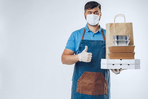 Delivery man in protective mask and medical gloves holding takeaway food. Compliance with the hygiene rules while covid-19 pandemic