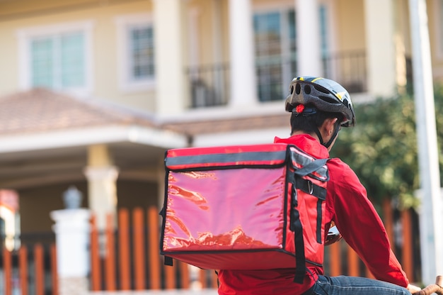 Photo delivery man in red uniform cycling to deliver products to customers at home.