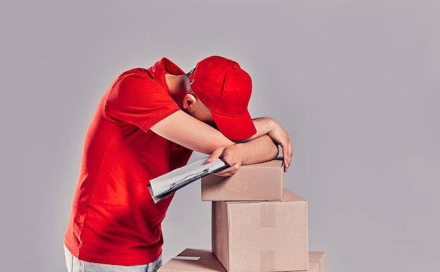 Delivery man in red uniform isolated on white background. male\
courier in cap, t-shirt holding pen, clipboard with papers\
document, blank empty sheet, cardboard box. receiving package. copy\
space