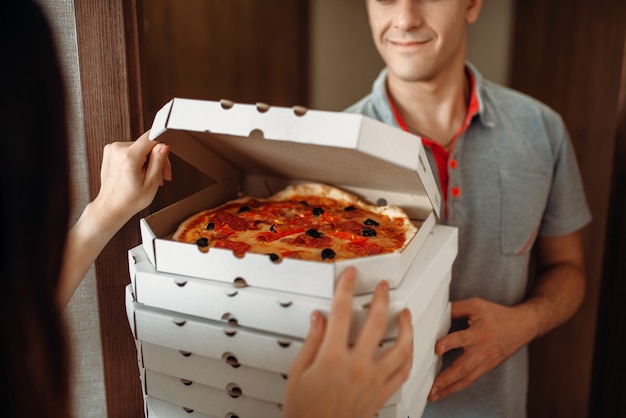 Delivery man shows fresh and hot pizza to female customer at the door