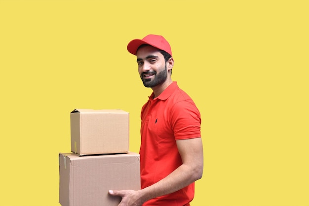 delivery man smiling in red t shirt and cap holding packaging box indian pakistani model