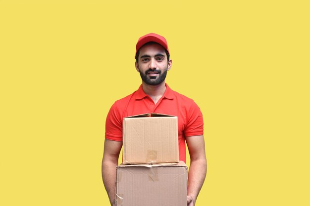 Photo delivery man smiling in red t shirt and cap holding packaging box indian pakistani model