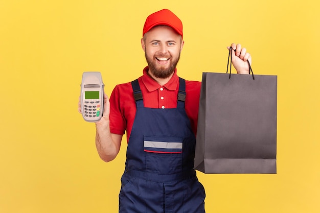 Delivery man standing with shopping bag and pos terminal looking at camera with positive expression