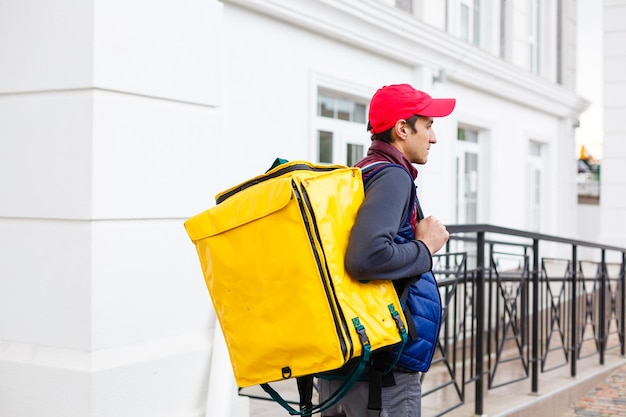 Photo delivery man standing with yellow thermo backpack for food delivery near the entrance home with empty space to copy paste