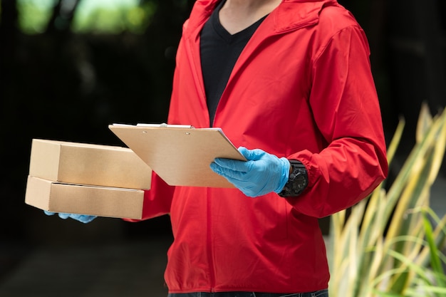 Фото Доставщик в синих перчатках и красной куртке, держа картонные коробки