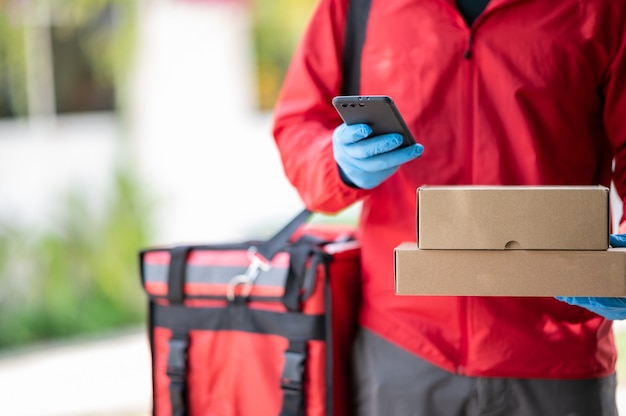 Photo delivery man wearing blue gloves in red cloth searching for customer address by mobile phone