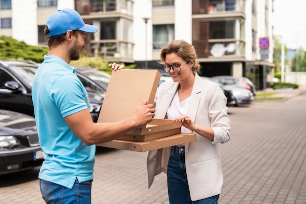 Delivery man wearing blue uniform delivers pizza to a woman clie