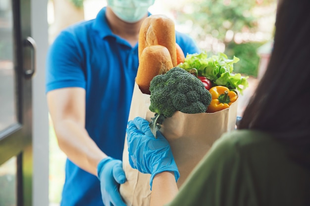 Delivery man wearing face mask and wear hygiene gloves in blue uniform handling bag of food