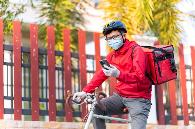 Delivery man wearing face protective mask to avoid corona virus Look at the phone to find the customer address through the application.