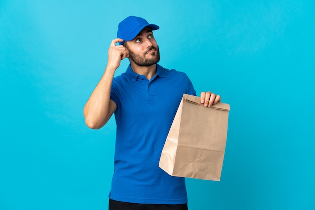 Delivery man with beard isolated on blue having doubts and with confuse face expression