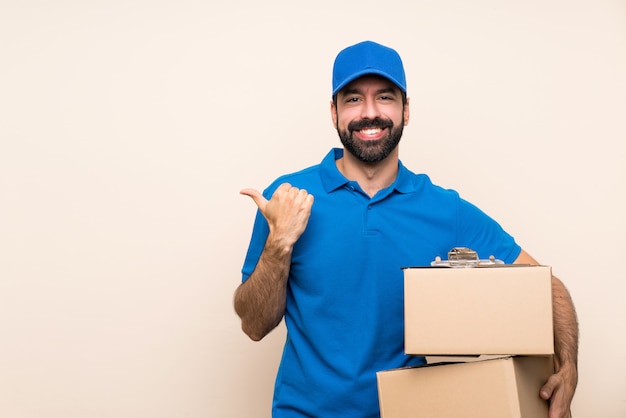 Delivery man with beard over isolated wall pointing to the side to present a product