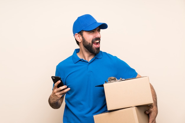 Delivery man with beard over isolated wall surprised and sending a message