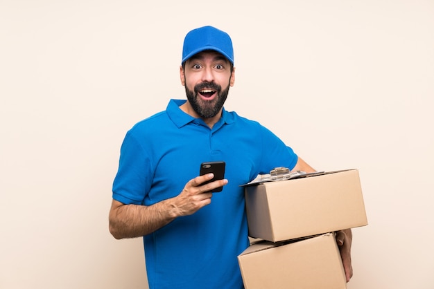 Delivery man with beard over isolated wall surprised and sending a message