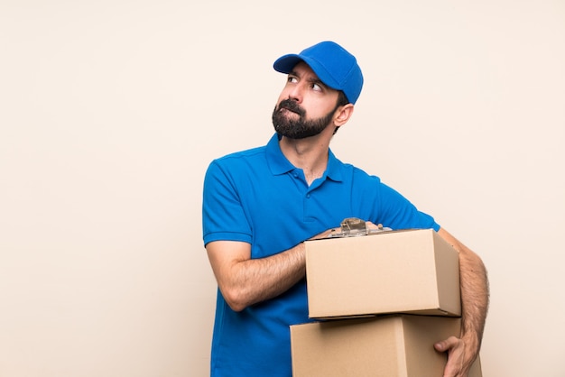 Delivery man with beard over isolated wall with confuse face expression