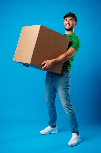 Delivery man with box in studio against blue background