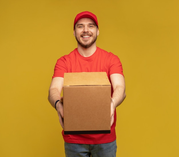 Delivery man with box in studio isolated on yellow wall