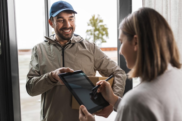 delivery man with box and woman signs digital form