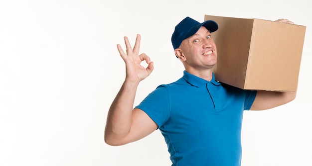 Photo delivery man with cardboard box on shoulder and okay sign