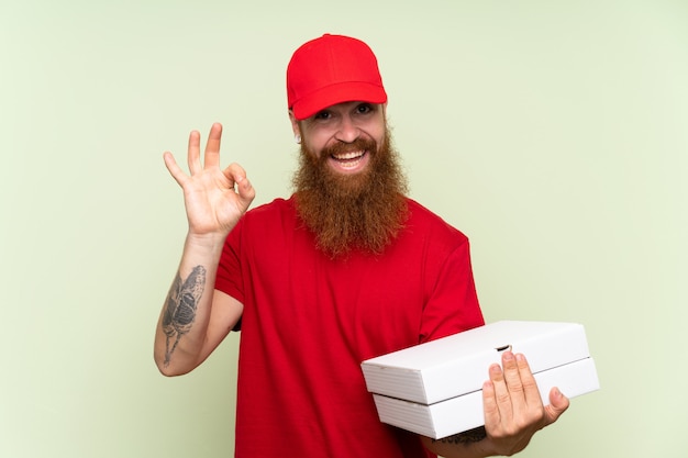 Delivery man with long beard over isolated green wall showing ok sign with fingers