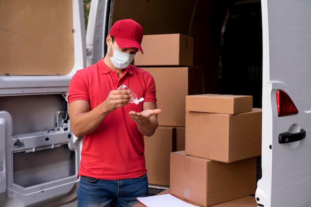 Uomo di consegna con maschera utilizzando disinfettante per le mani