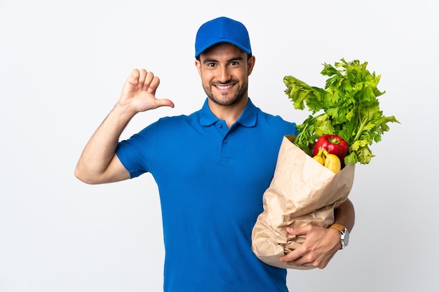 Delivery man with vegetables isolated on white proud and self-satisfied