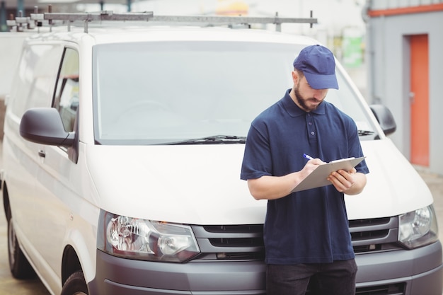 Delivery man writing on clipboard in front of his van