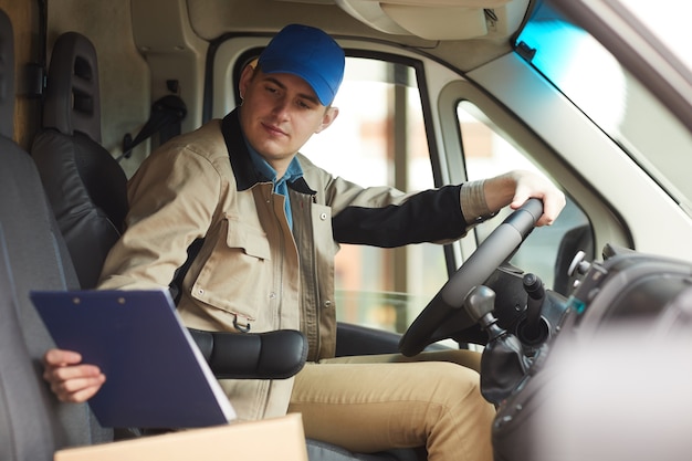Foto addetto alle consegne che controlla l'indirizzo di consegna durante la guida del furgone