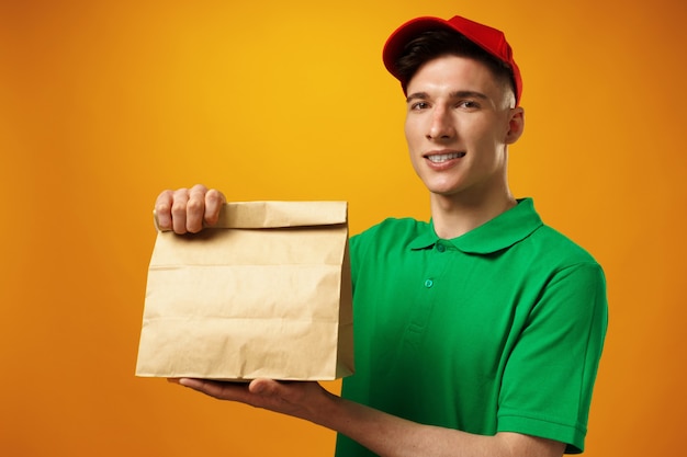 Delivery person holding parcel with food delivery against\
yellow background