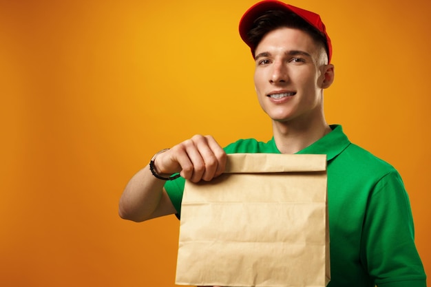 Доставщик, держащий посылку с доставкой еды на желтом фоне