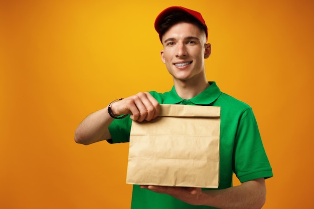 Delivery person holding parcel with food delivery against\
yellow background