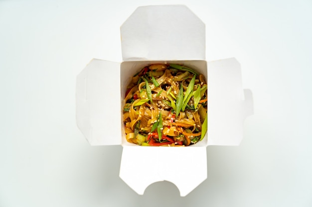 Delivery of ready-made Asian food. noodles with vegetables and seafood in a white box. Delicious dinner. order food over the phone or online. sushi sticks.