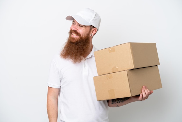 Delivery reddish man isolated on white background looking to the side and smiling