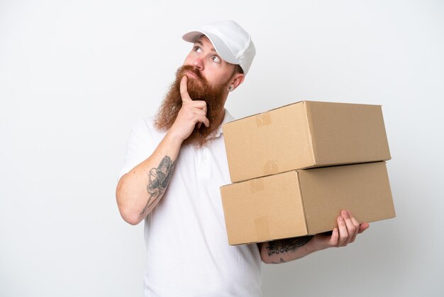 Delivery reddish man isolated on white background looking up while smiling