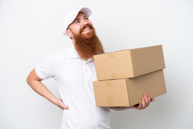 Delivery reddish man isolated on white background posing with arms at hip and smiling