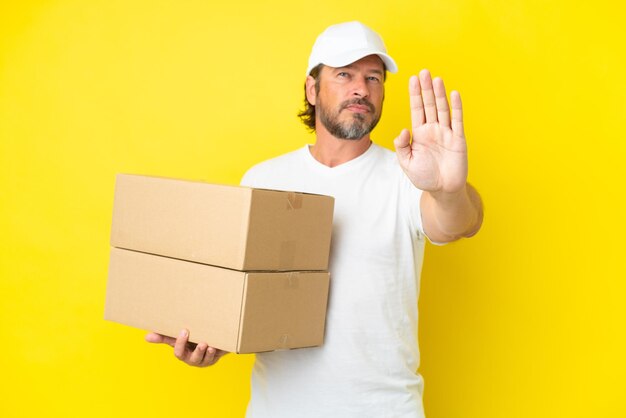 Delivery senior dutch man isolated on yellow background making stop gesture