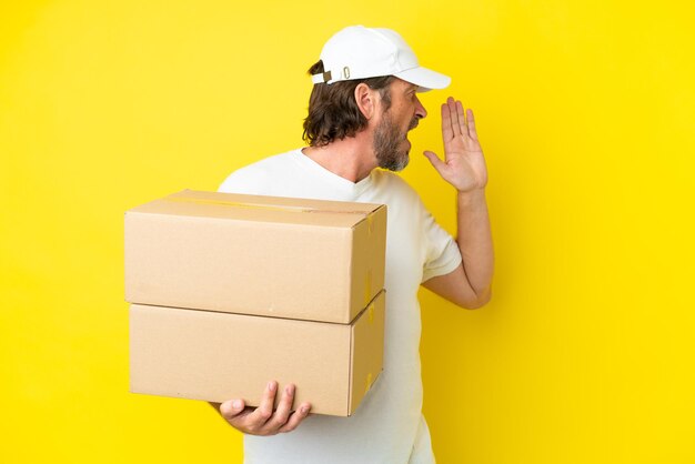 Delivery senior dutch man isolated on yellow background shouting with mouth wide open to the side