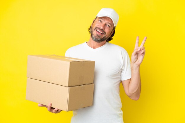 Delivery senior dutch man isolated on yellow background smiling and showing victory sign