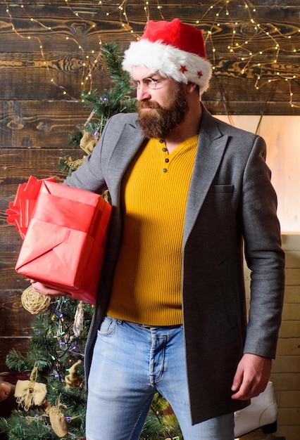 Servizio di consegna lo spirito del natale è qui diffondere felicità e gioia ragazzo barbuto indossare cappello di babbo natale portare scatola regalo di natale consegna regalo di natale regalo di natale uomo cappello da babbo natale tenere regalo