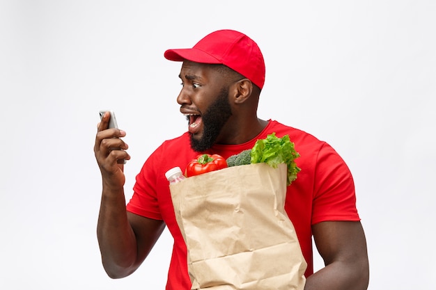 Delivery service: Handsome african delivery man talking to mobile with shocking facial expression.