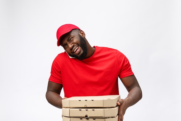 Delivery service: Handsome african pizza delivery man talking to mobile with shocking facial expression.  