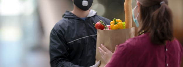 Photo delivery service man handing over fresh food bag to female customer