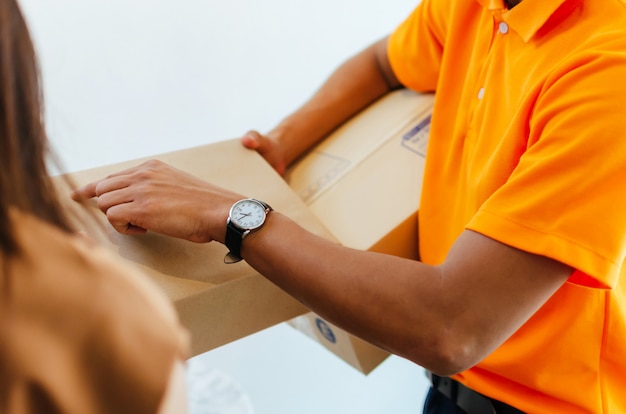 Uomo di servizio di consegna in uniforme arancione con il cliente della donna che riceve la scatola del pacchetto pacchi postali dal corriere a casa, spedizione merci, servizio di consegna espresso veloce, shopping online, concetto logistico