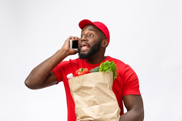 Delivery service - Portrait of Handsome African American delivery man or courier with grocery package and talking on mobile phone to check the order.  