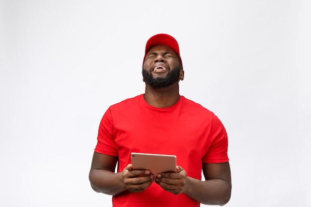 배달 서비스-어리석은 공격적인 표현과 불행한 태블릿으로 심각한 아프리카 계 미국인 배달 남자의 초상화.