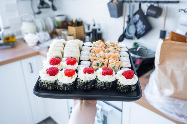 delivery of sushi and rolls set is hold in hand in the interior modern kitchen of house