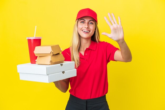 Delivery Uruguayan woman holding fast food isolated on yellow background counting five with fingers