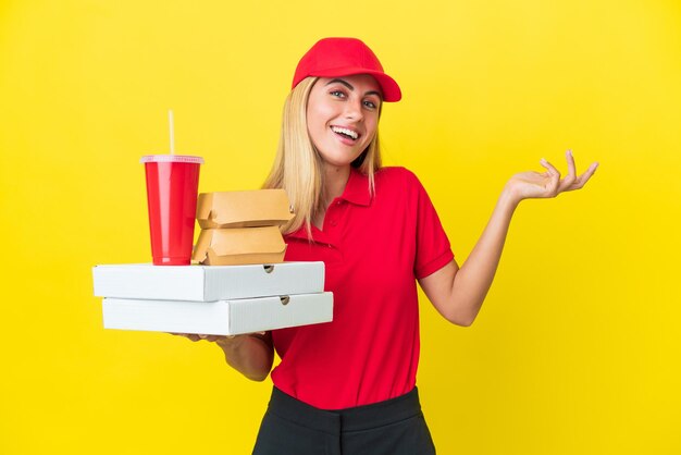 Delivery Uruguayan woman holding fast food isolated on yellow background extending hands to the side for inviting to come