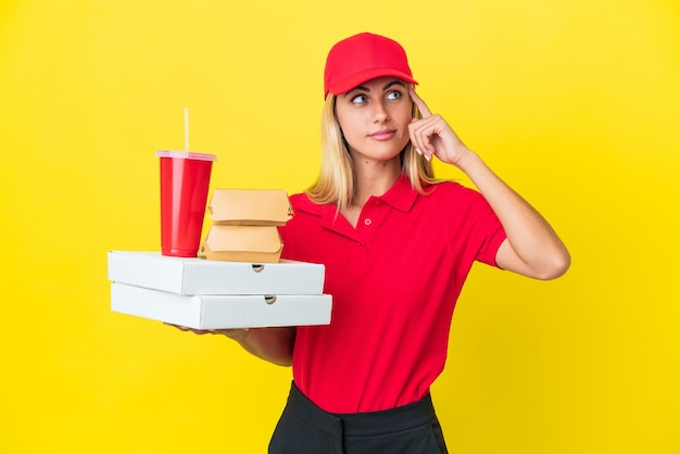 Delivery Uruguayan woman holding fast food isolated on yellow background having doubts and thinking