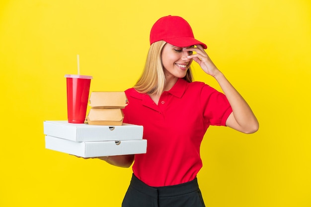 Delivery Uruguayan woman holding fast food isolated on yellow background laughing